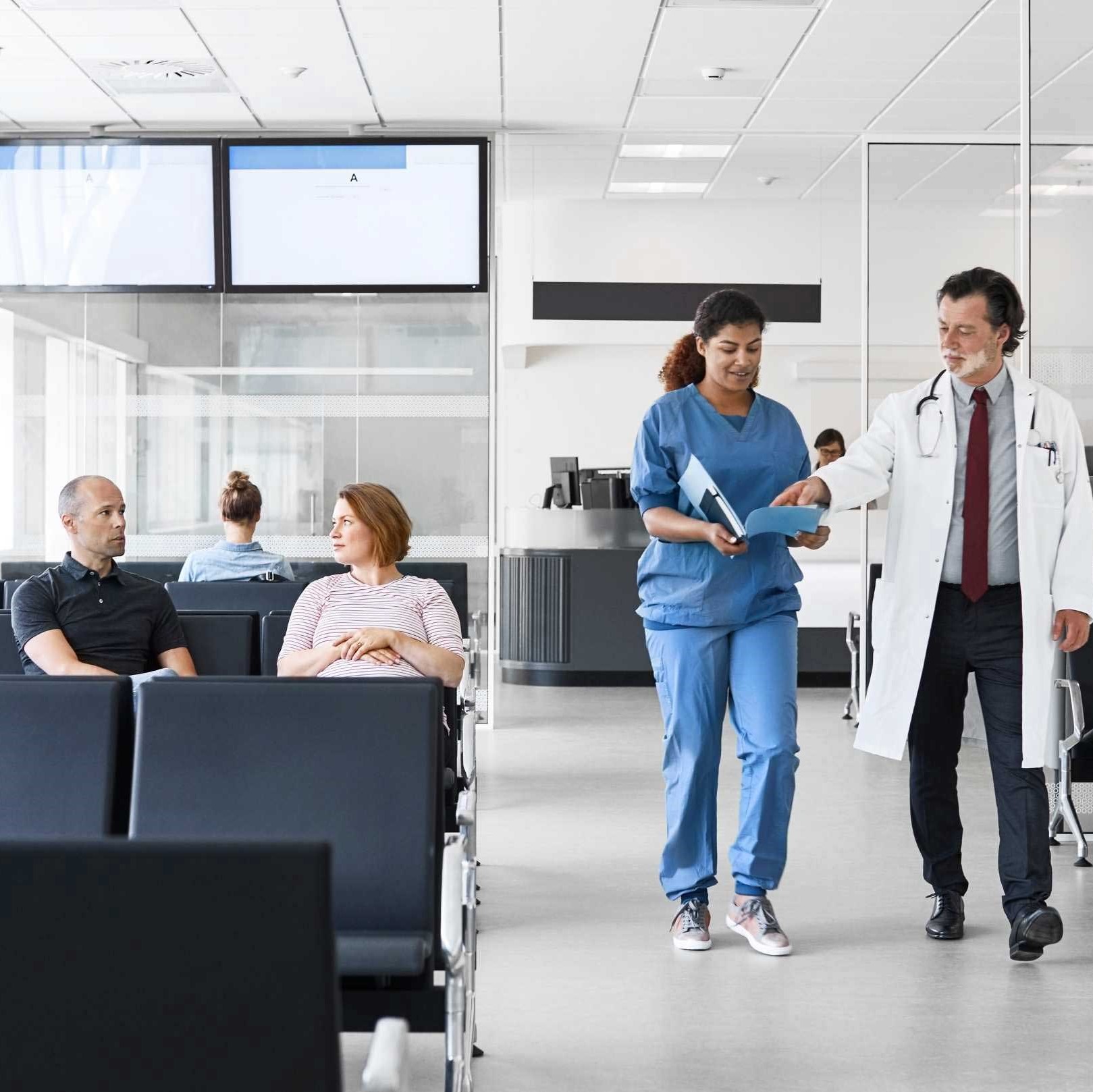 Doctor And Nurse Walking By Patients In Lobby Square